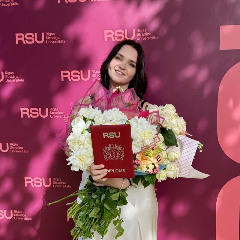 RSU SZF absolvente Anastasija Kovaļenko izlaiduma dienā ar ziediem un diplomu