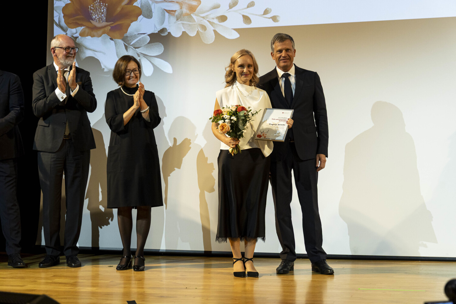 RSU aulā uz skatuves priekšplānā stāv Dagnija Briede un RSU kanclers Toms Baumanis