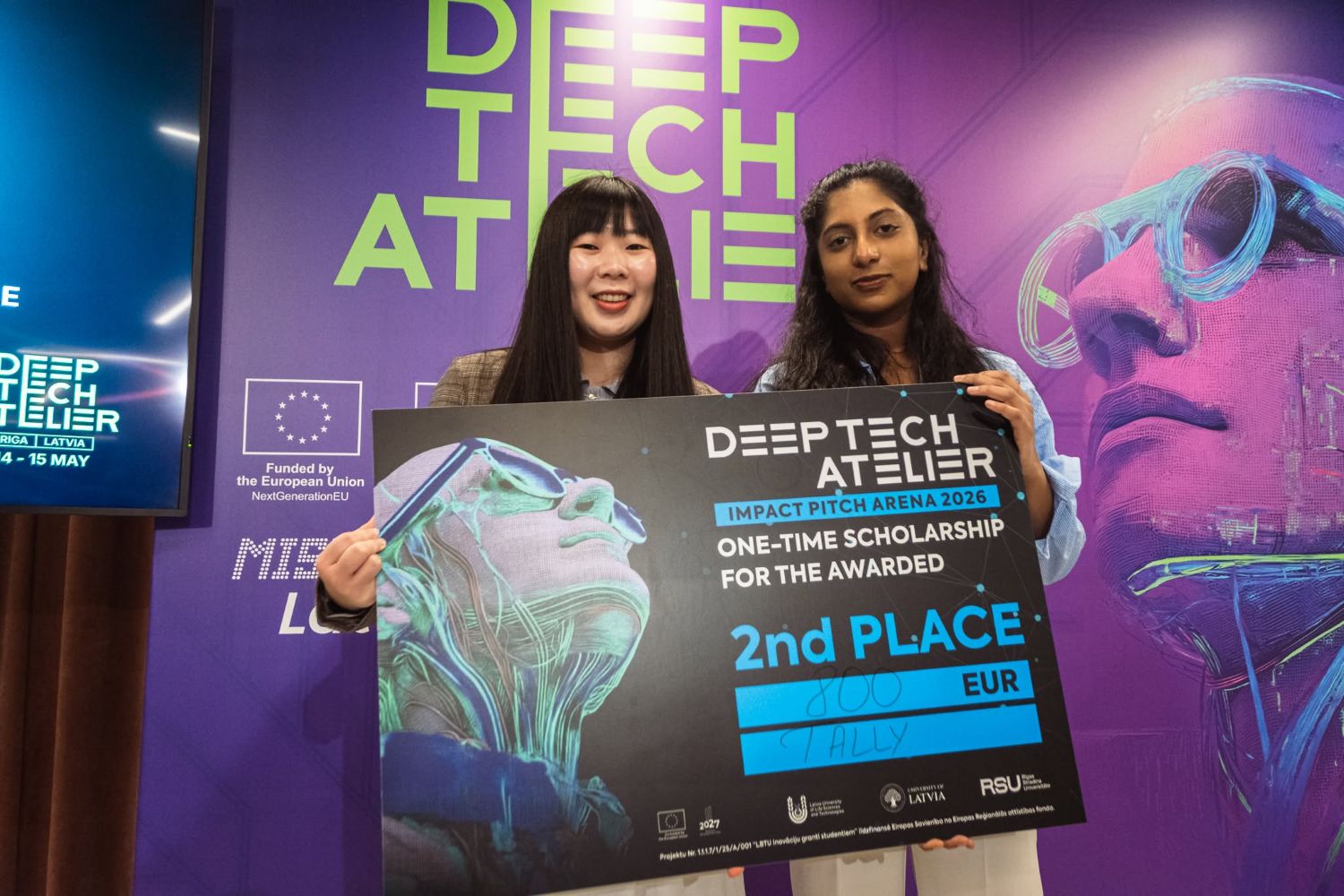 Komanda TALLY ieguva 2. vietu “Deep Tech Atelier” organizētajā “Pitch arena”. Abas TALLY komandas dalībnieces pēc pasākuma stāv ar saņemto atzinību rokās.