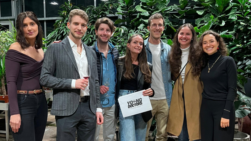 Seven students posing in front of greenery, Simona Costa centre, holding a sign that says Young Doctors