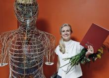 Resident Unda Jukone posing with her diploma next to a anatomical figure featuring the nervous system
