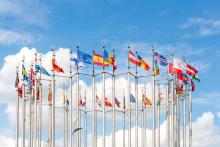 Group of flags of European countries waves against blue sky with few clouds.